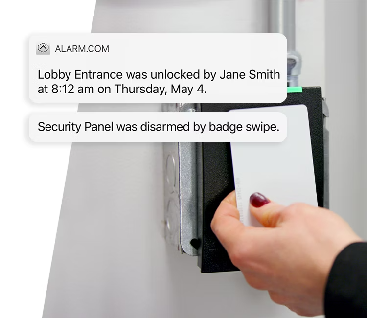 Hand swiping a white security badge at a reader with Alarm.com notifications showing a door unlock event.