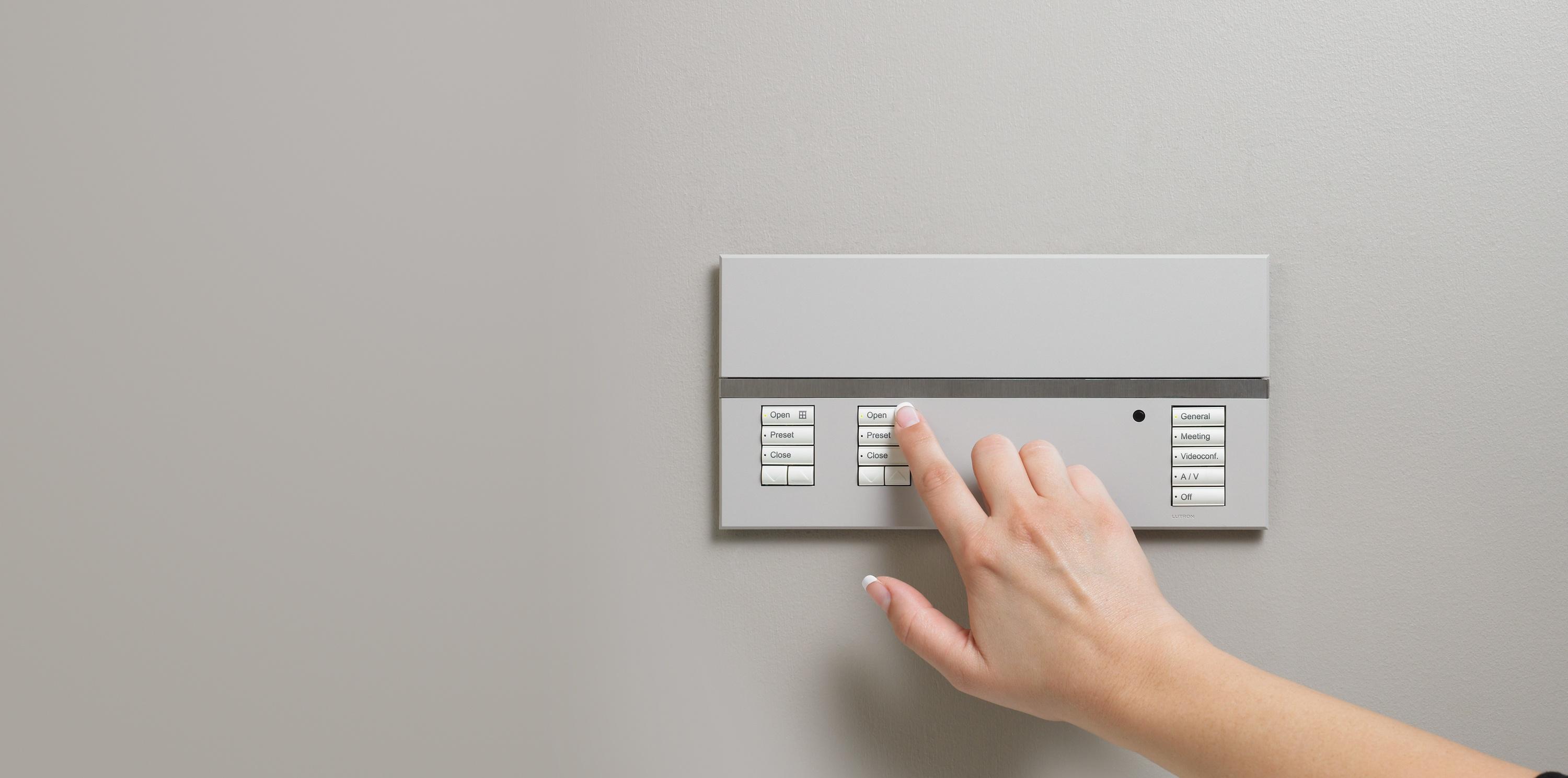 Person pressing a button on a modern wall-mounted control panel with labeled settings for lighting or room automation.