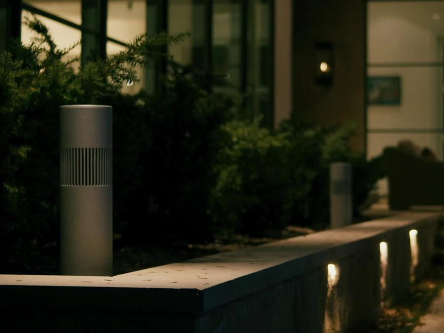 An outdoor speaker in a dimly lit garden outside of a modern-looking house.