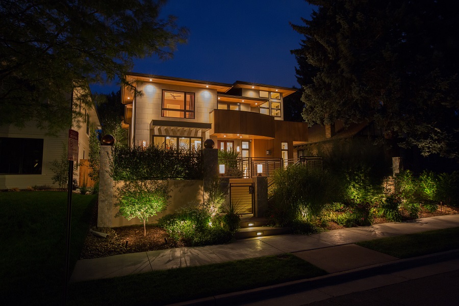 Modern two-story home at night with lit windows, warm exterior lights, and landscape lighting along the front walk.