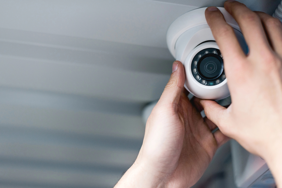 Close-up of a person’s hands installing or adjusting a white dome security camera on a ceiling.
