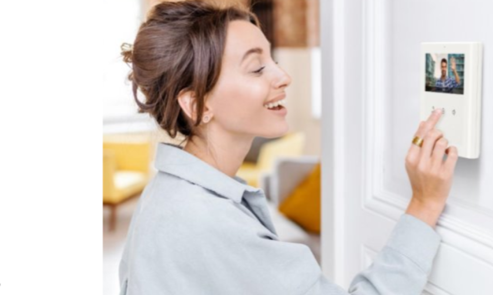 Woman smiling while using a wall-mounted video intercom to see a visitor on the screen at her front door.