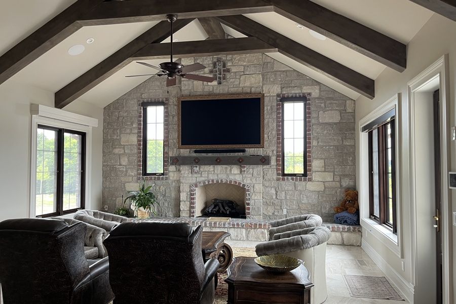 Samsung Frame TV mounted above a stone fireplace in a vaulted living room with wood beams and built-in speakers.