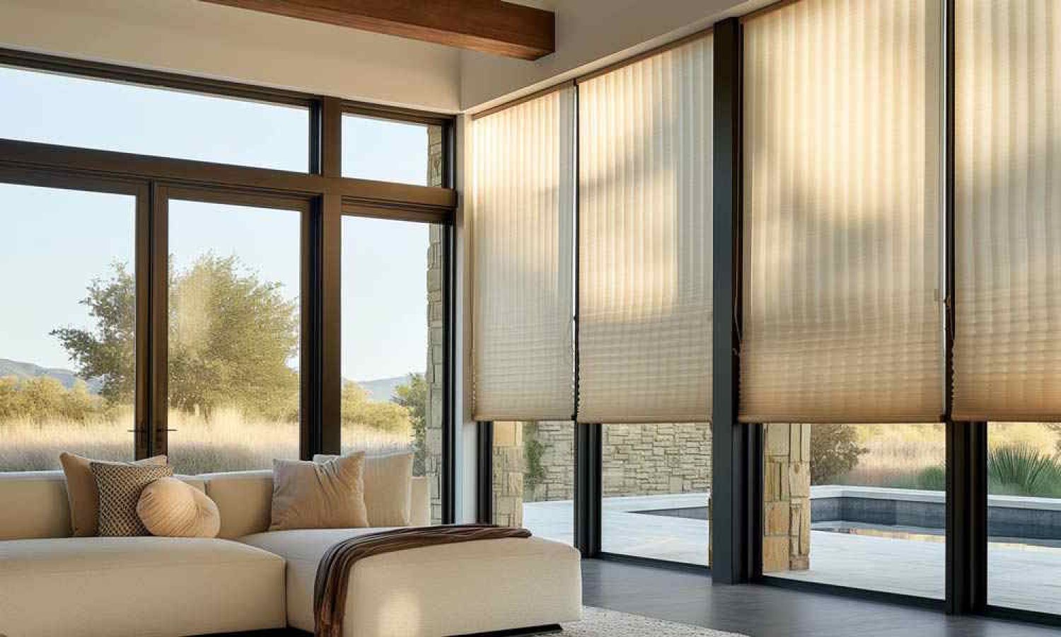 A modern living room with large floor-to-ceiling windows featuring motorized shades partially lowered to control natural light while maintaining views of the outdoor landscape.
