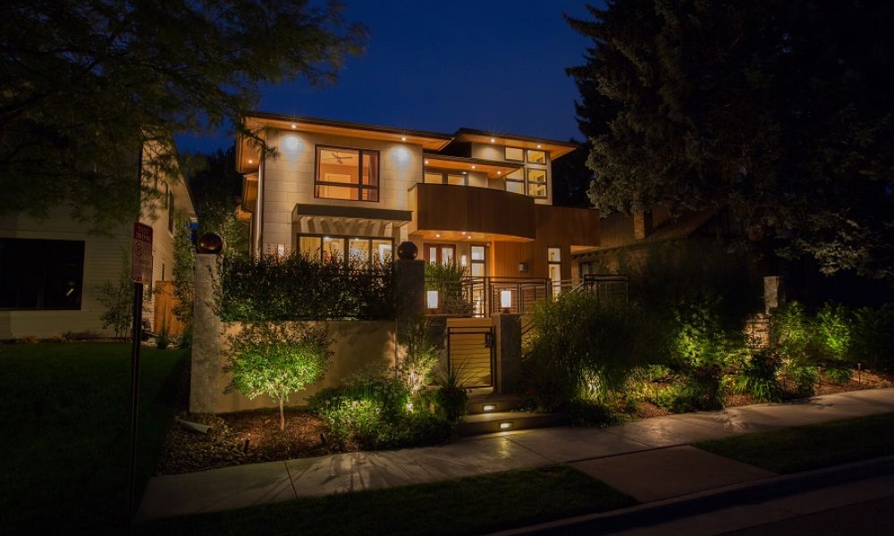 Modern two-story home at night with lit windows, warm exterior lights, and landscape lighting along the front walk.