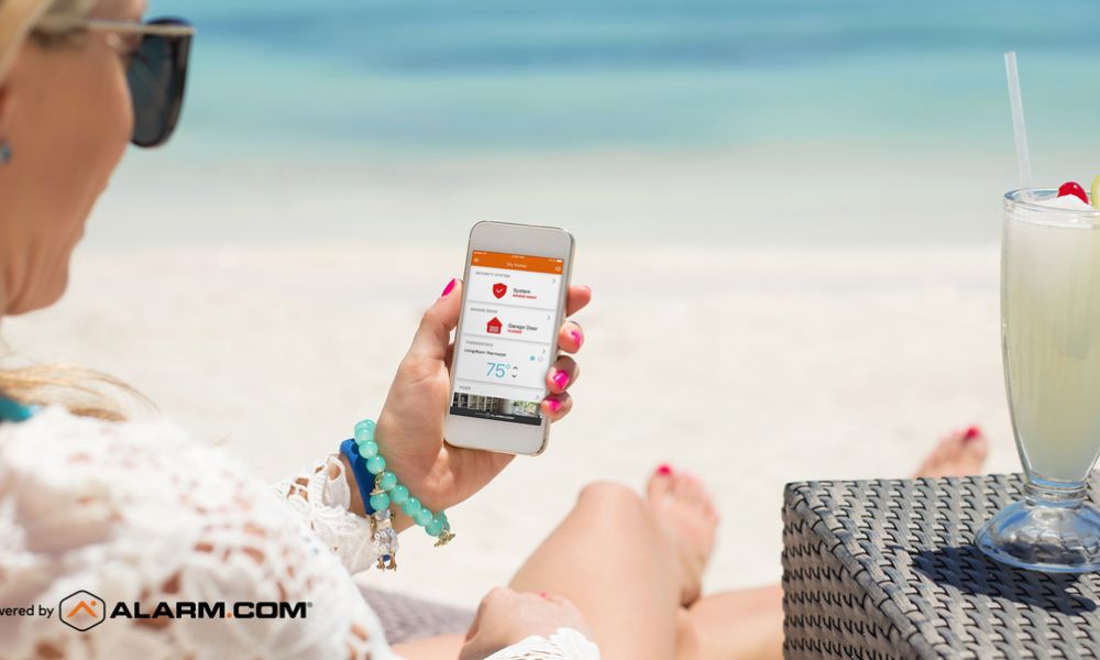 Woman relaxing on a beach chair using the Alarm.com mobile app on her smartphone to monitor home security.