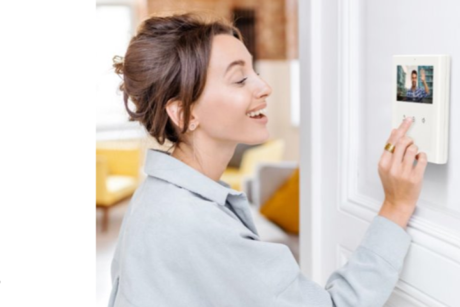 Woman smiling while using a wall-mounted video intercom to see a visitor on the screen at her front door.