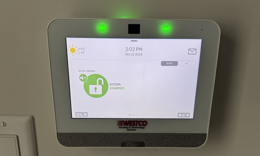 A Westco Security touchscreen control panel mounted on a wall displaying a disarmed status and green LED indicator lights.