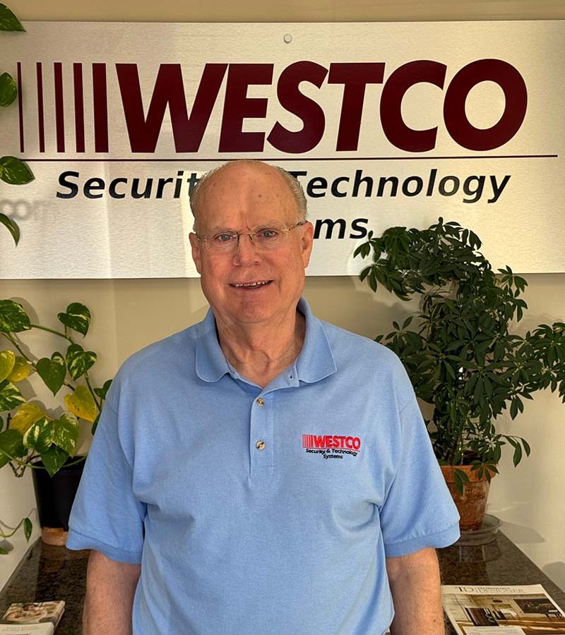A professional headshot of a middle-aged man in a suit, smiling against a neutral background.