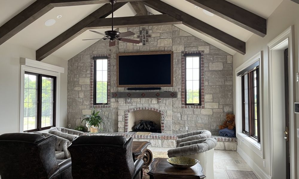 Samsung Frame TV mounted above a stone fireplace in a vaulted living room with wood beams and built-in speakers.
