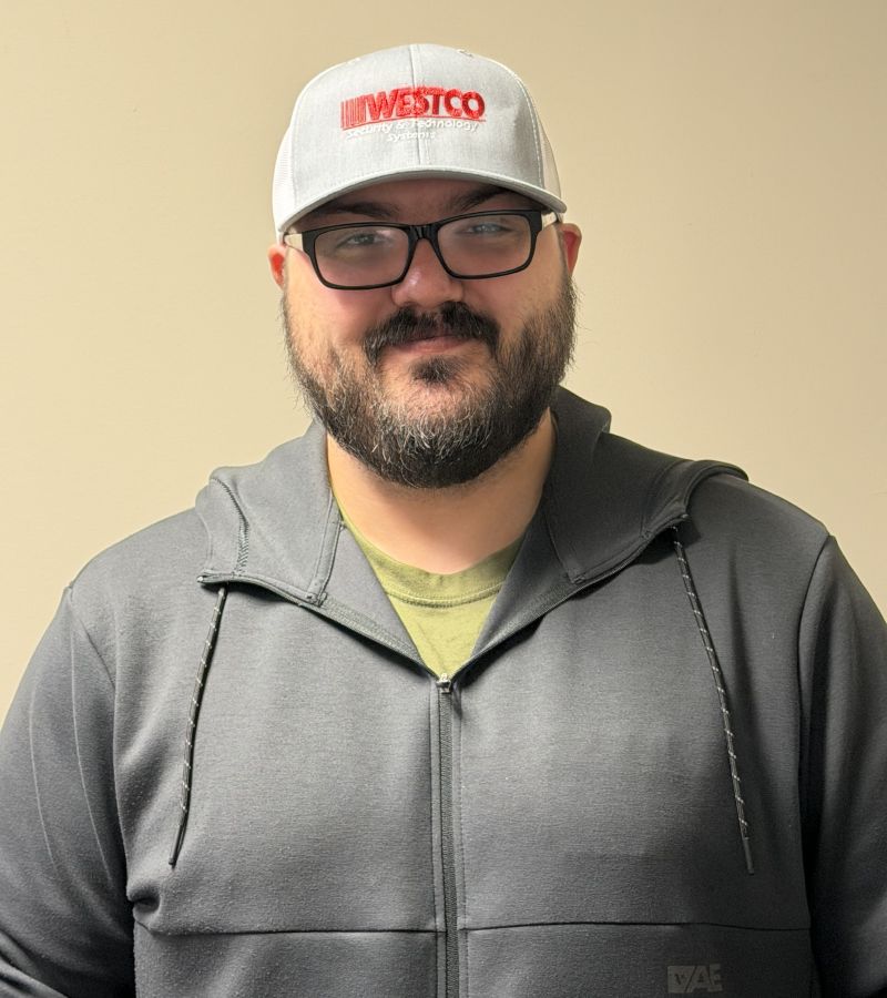 A man wearing a black  jacket, grey cap, and glasses.