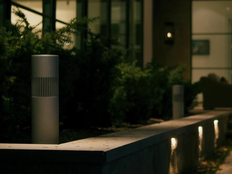 An outdoor speaker in a dimly lit garden outside of a modern-looking house.